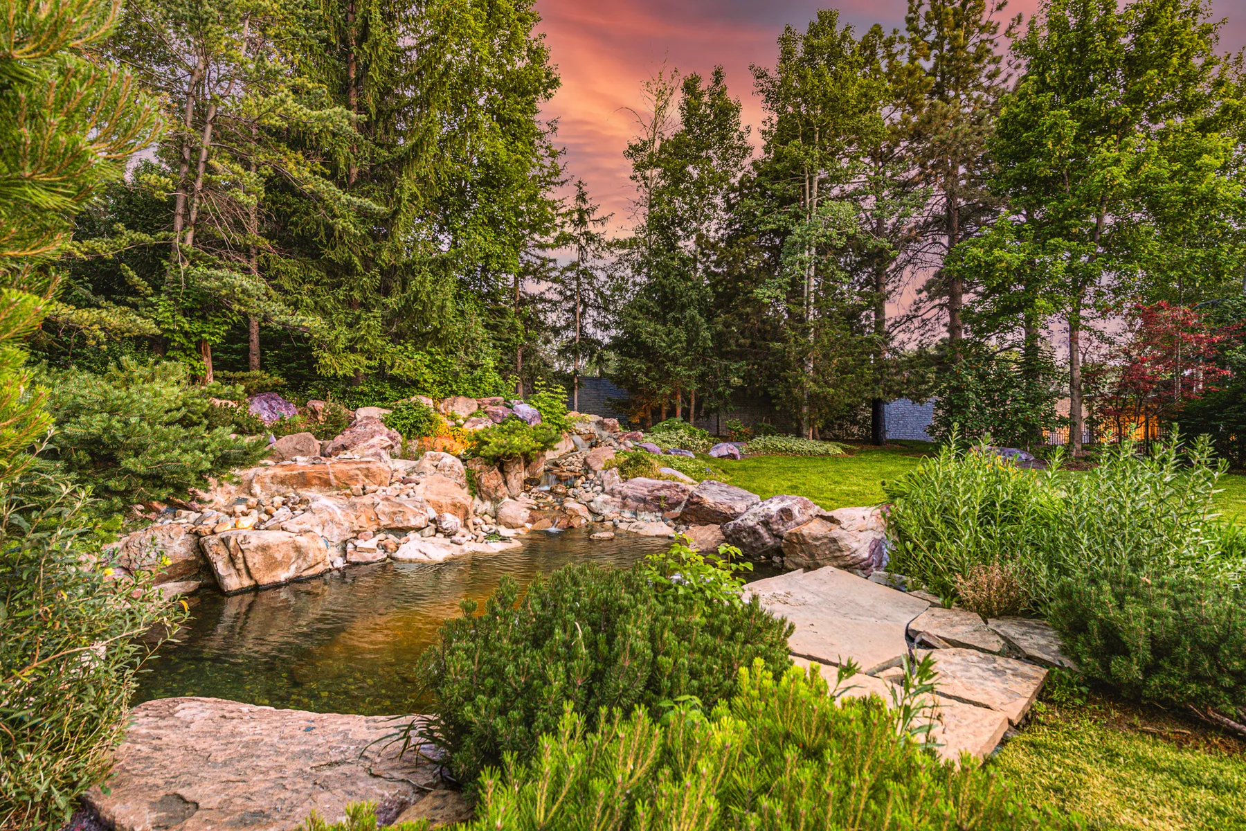 Landscaped water feature and lawn beneath a twilight sky